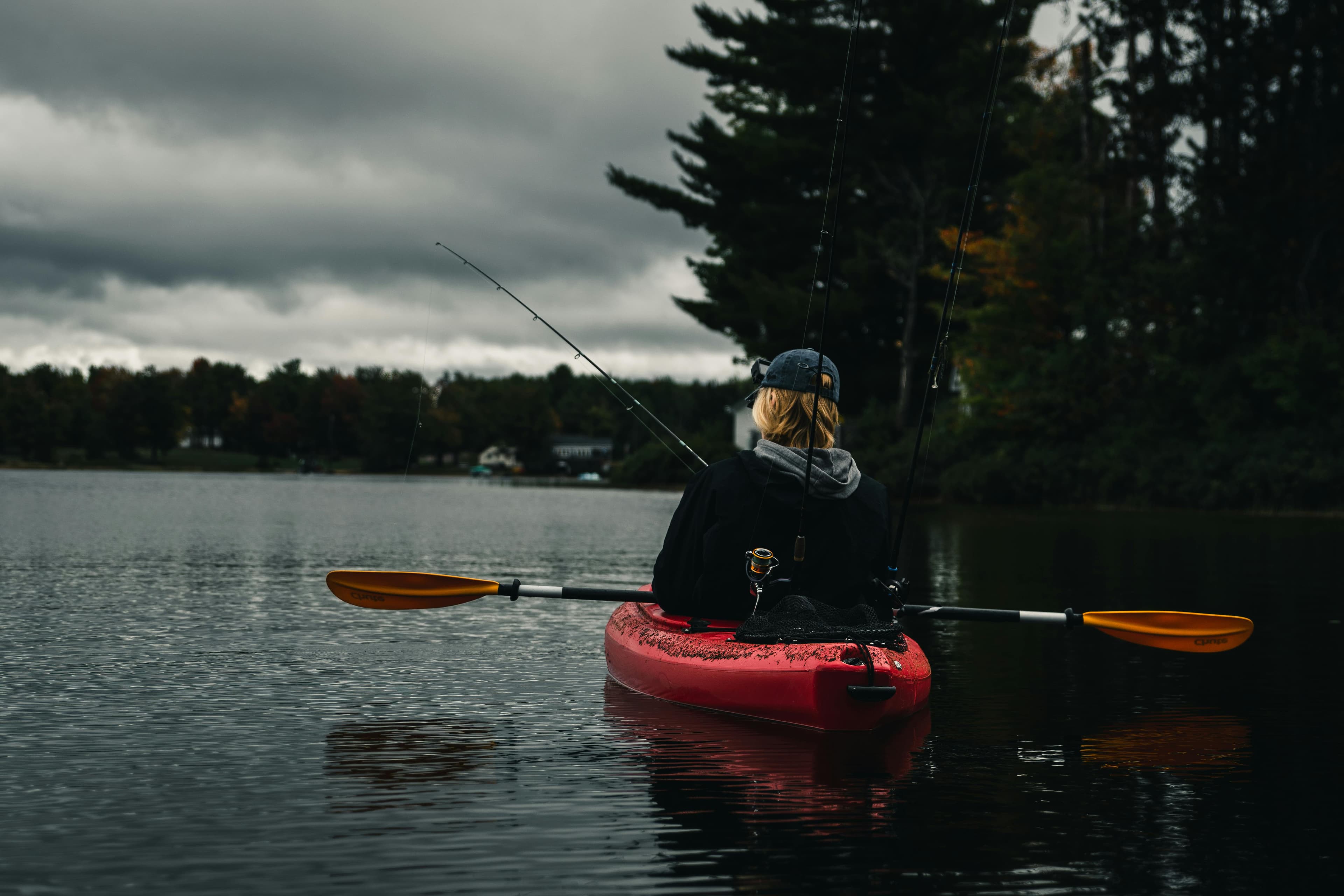 Angler fishing at dawn on a misty lake with kayaks beached on the shore