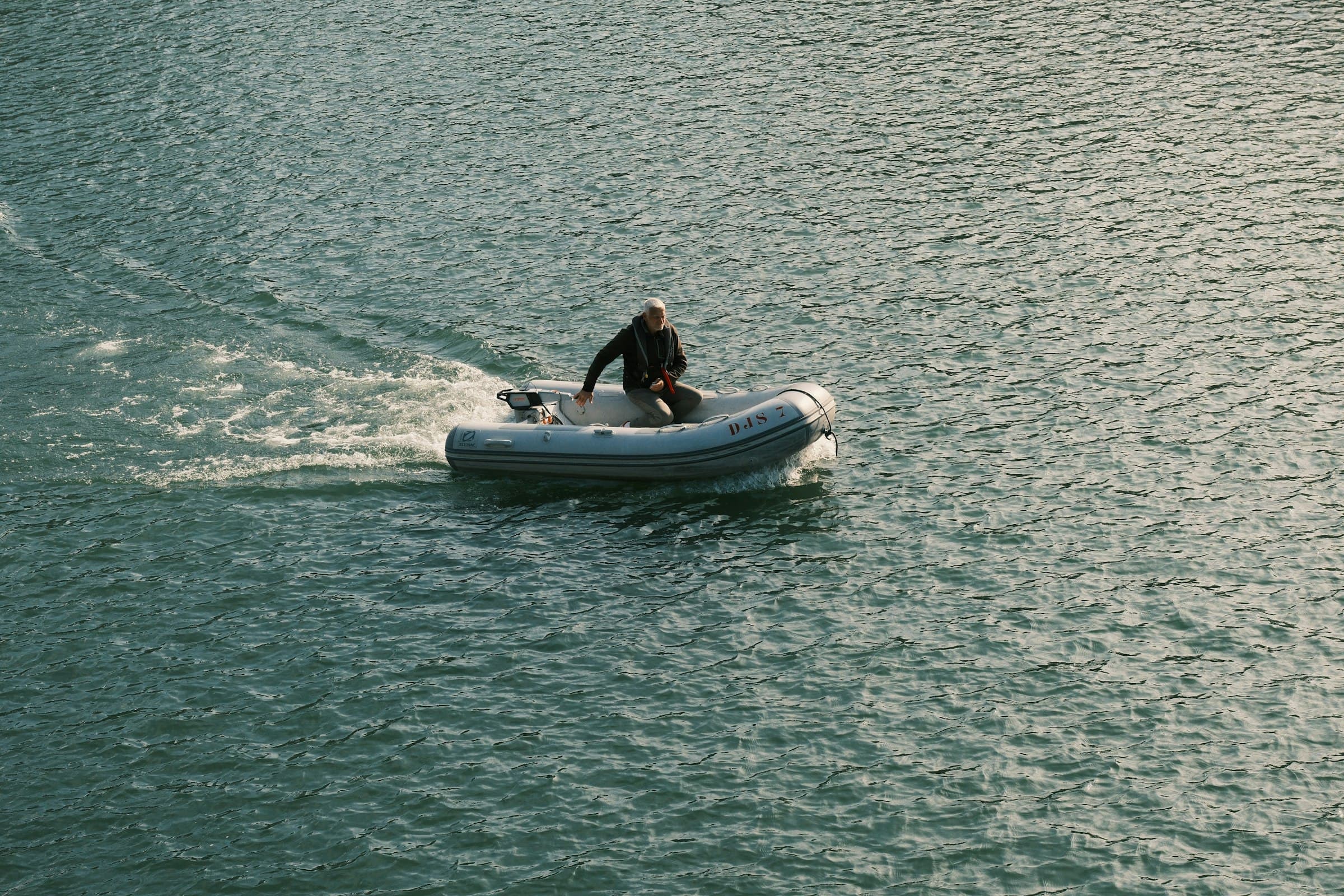 A person driving a small motorized inflatable boat across open water