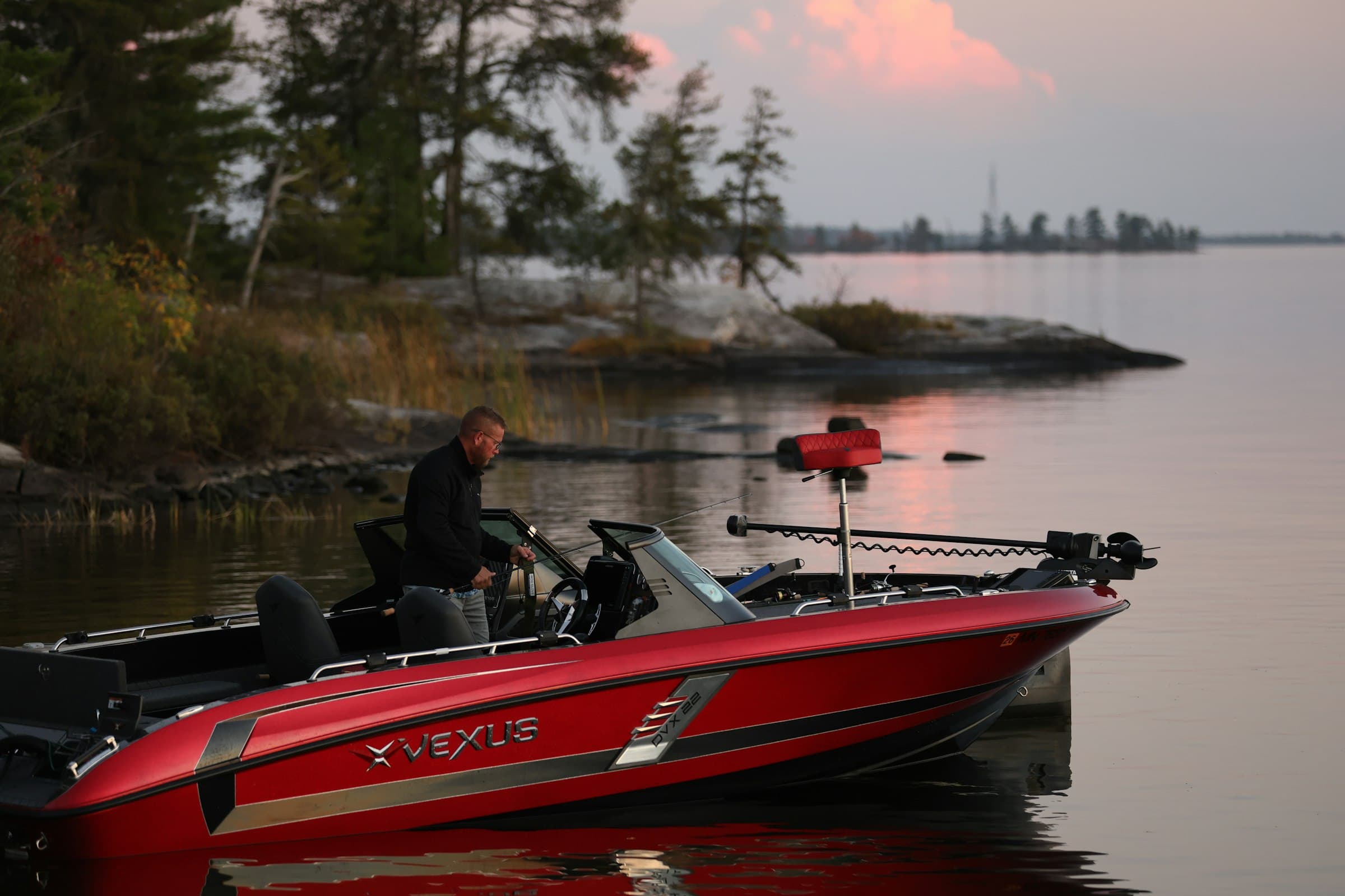 A red fishing boat at dawn with a bow-mount trolling motor stowed on the deck